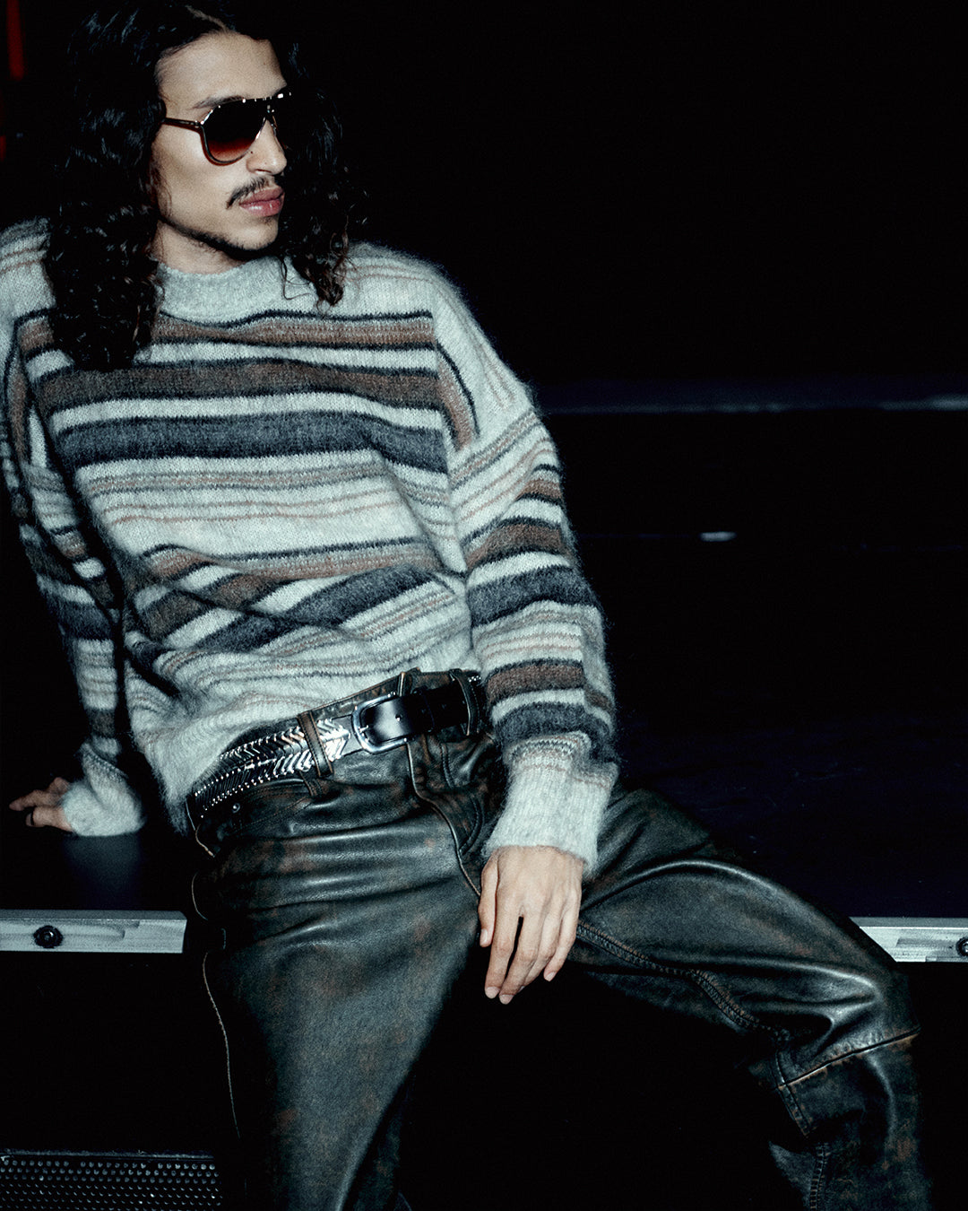 Men seats on the bar wearing a stripped jumper and leather pants.