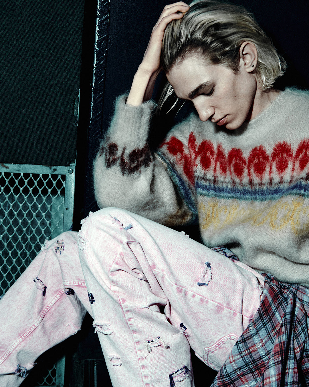 Men seats on the ground wearing patterned jumper and pink denim.