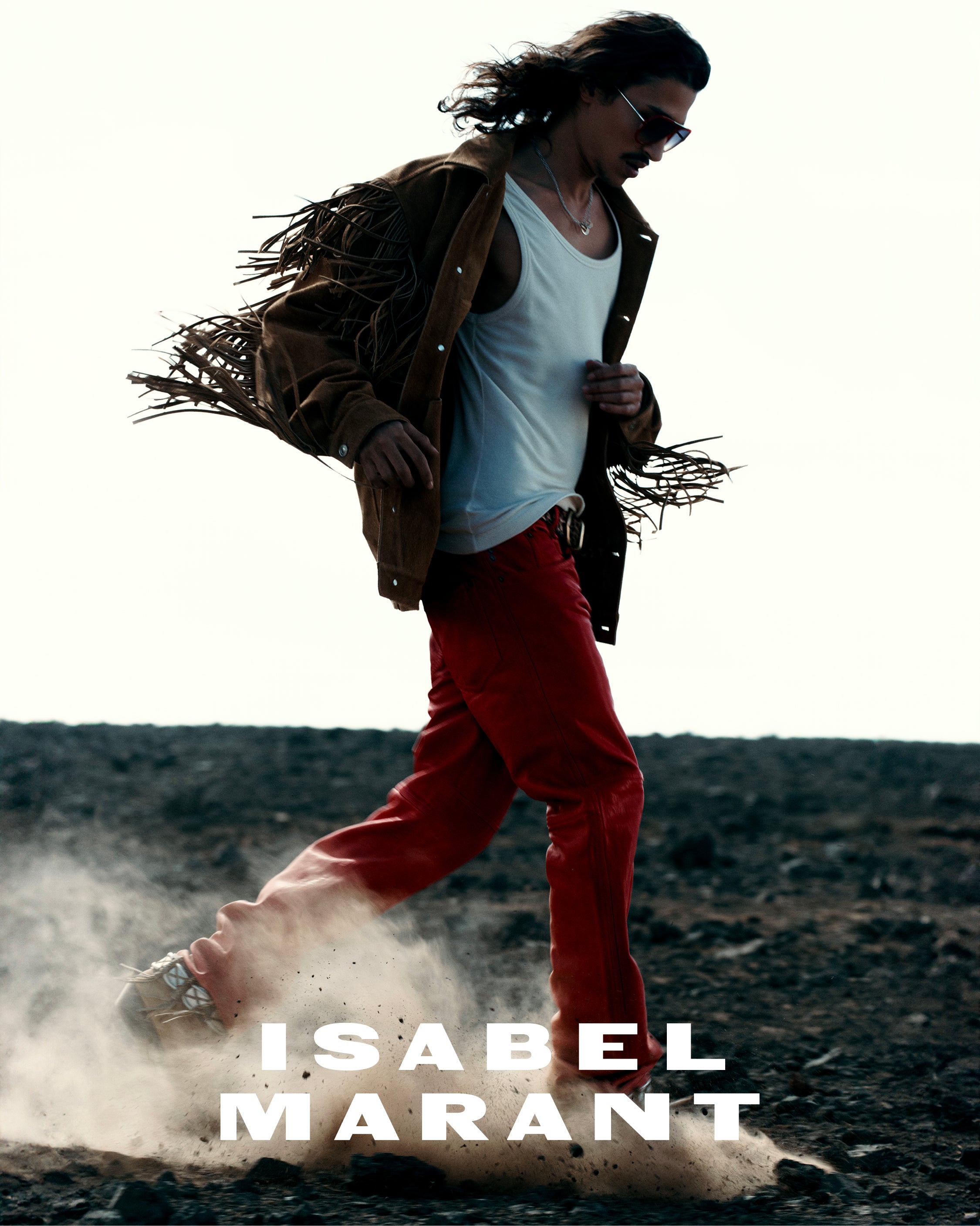 Men model running in the desert wearing a fringe suede jacket and red pants.