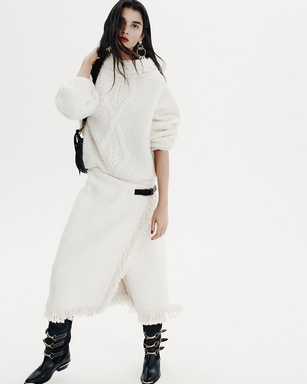 White background the model is posing with full white look : a bug sweater and long skirt accompany with leather black boots.