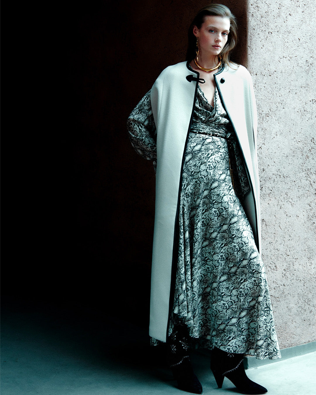 Feminine model, dressed in the Emilina long cape in ecru wool and cashmere, the Zarga blouse in printed silk with pleats, the Sakura long skirt in printed silk and black ankle boots.