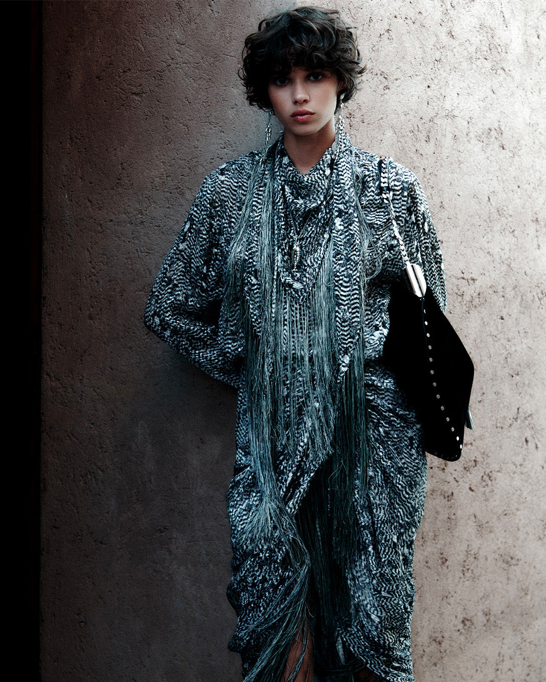 Feminine model, dressed with the Ilda Shirt in black and ecru burnt velvet, the Roany Draped Skirt in black and ecru burnt velvet with bangs and the Oskan Tassel Shoulder Bag in black and silver burnt calf leather.