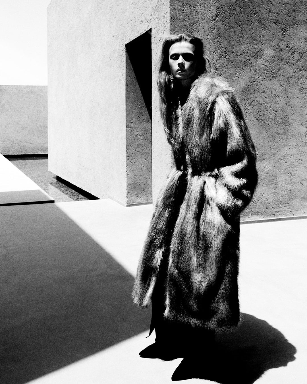 Feminine model, dressed with the fur-effect Alberta long coat and the Nadela long dress in black jersey.