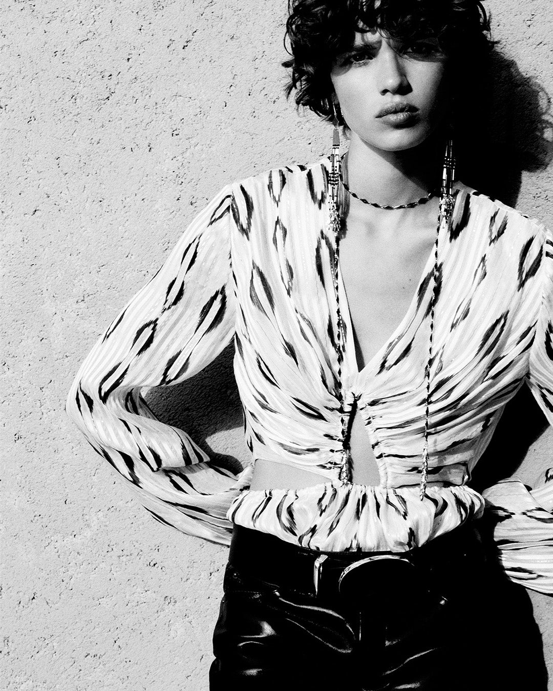 Feminine model, dressed in a Stelar openwork blouse in ecru and black graphic silk, Dolena slim black leather pants, Leonie belt and Olathe earrings