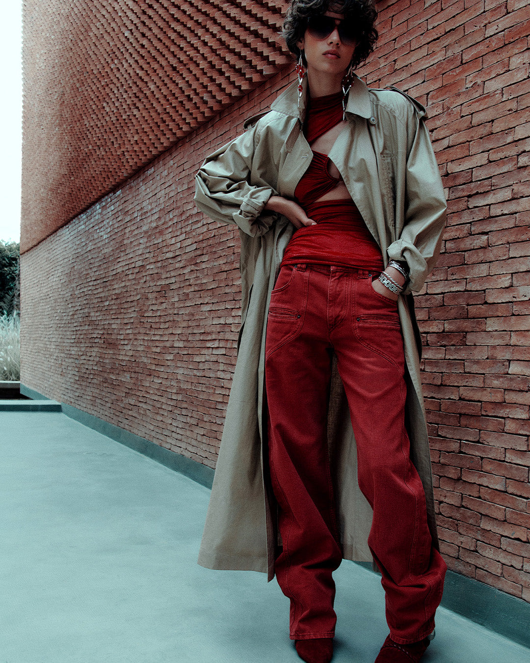Feminine model, dressed in a long trench coat, a red top and jeans, and boots with a small red heel.