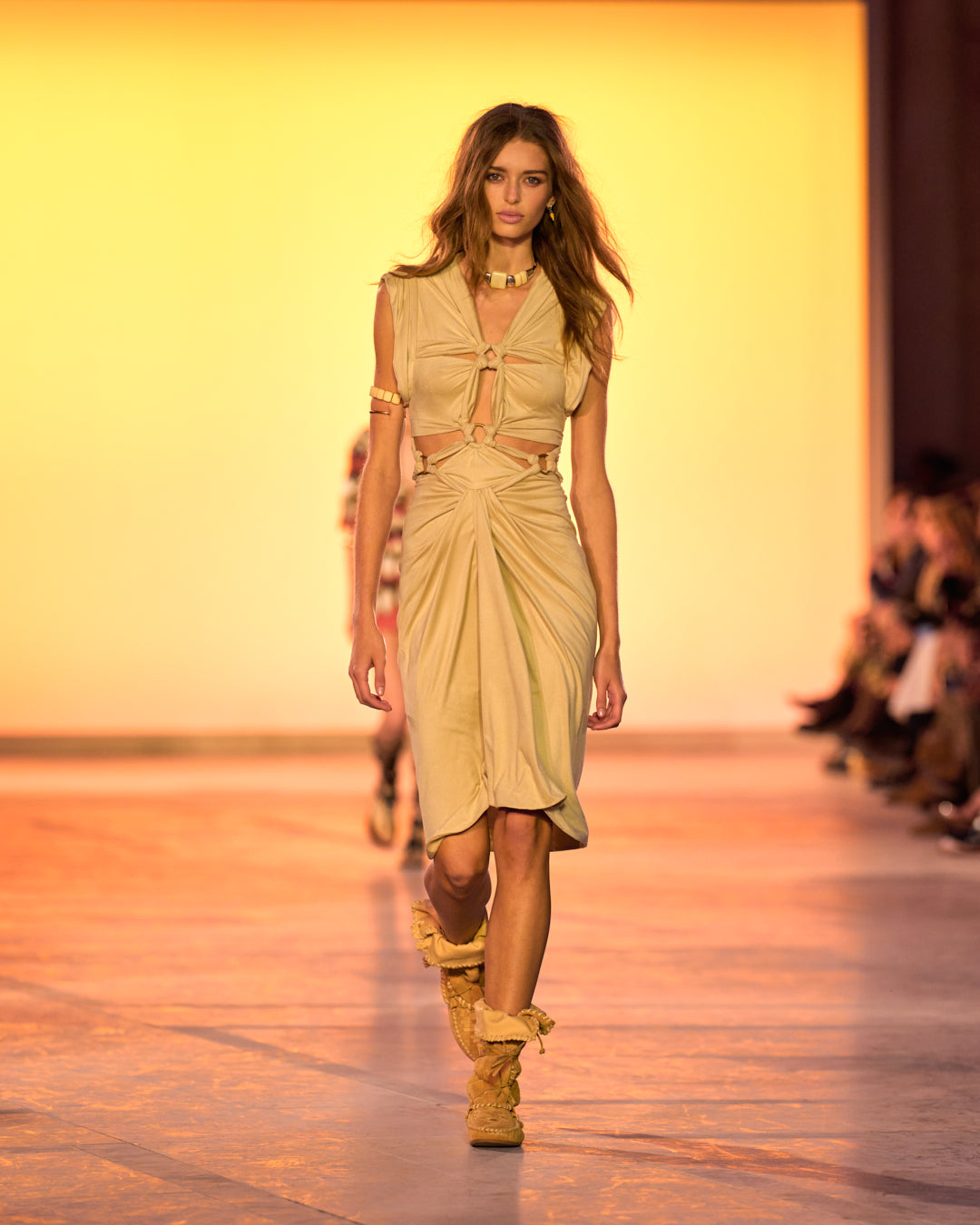 Female model on the catwalk, wearing the Sirena dress in draped suede faux leather, Winki boots in suede and braided leather and the Paradise choker necklace in pearls.