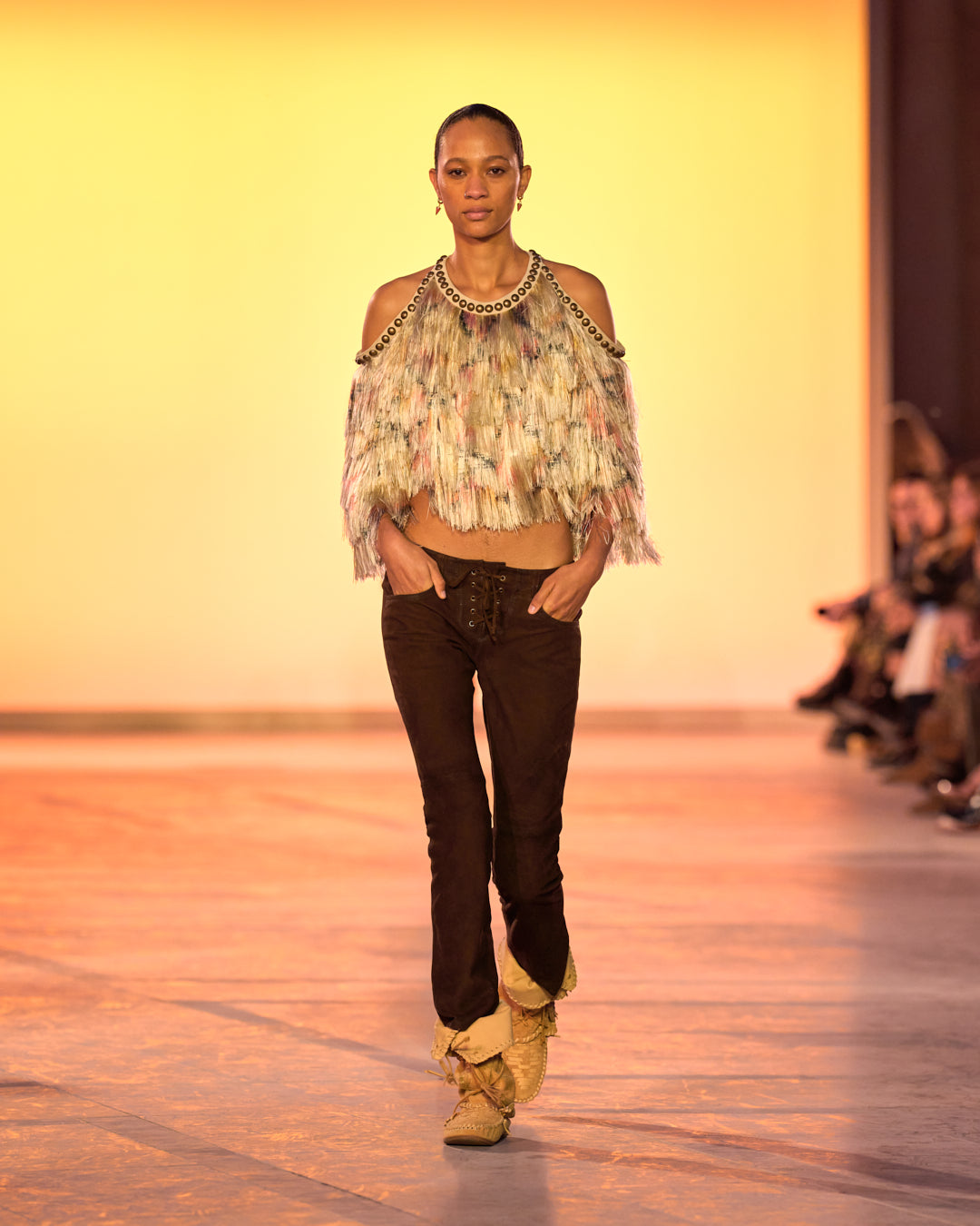 Female model on the catwalk, wearing a feather-effect fringed top, Vanel lace-up pants in suede and Winki boots in suede and braided leather.