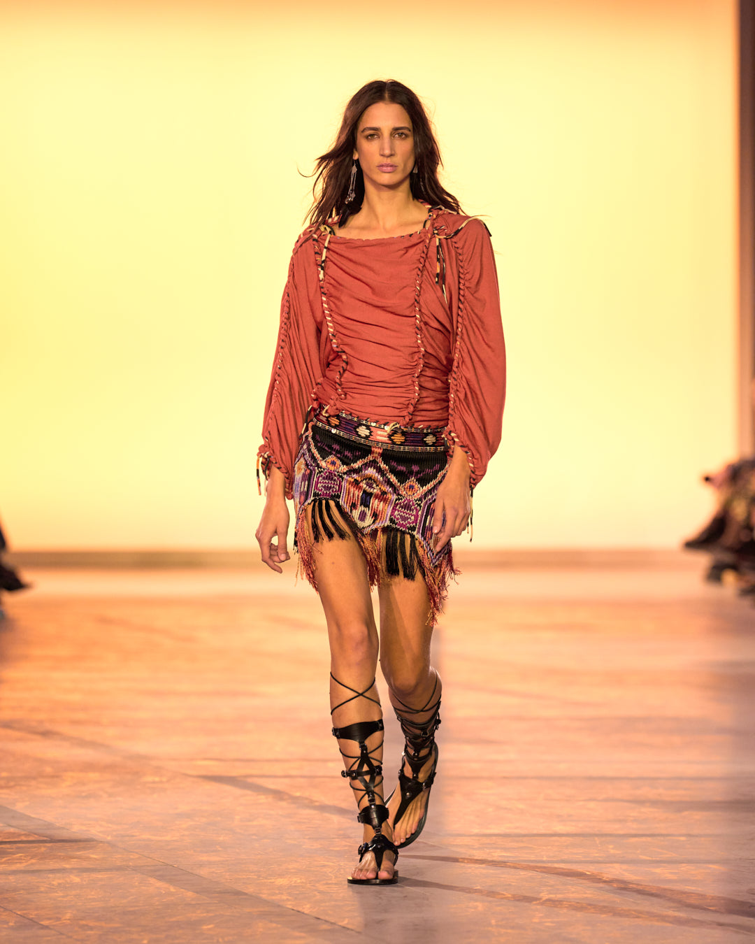 Female model on the catwalk, wearing a braided jersey top, fringed embroidered Yolana skirt and black sandals.