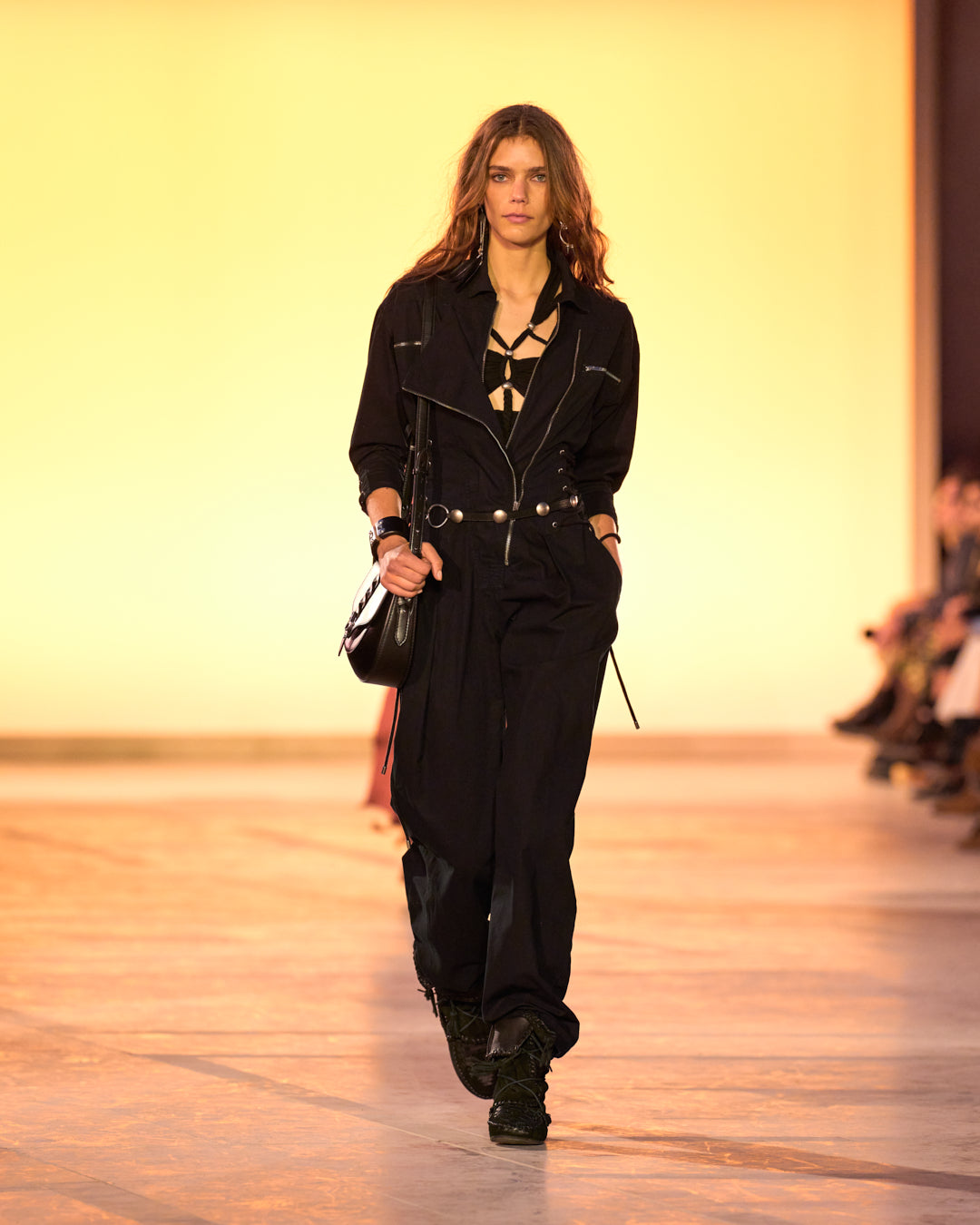 Female model on the catwalk, dressed in a black jumpsuit, black altay bag and black suede and braided Winki boots.