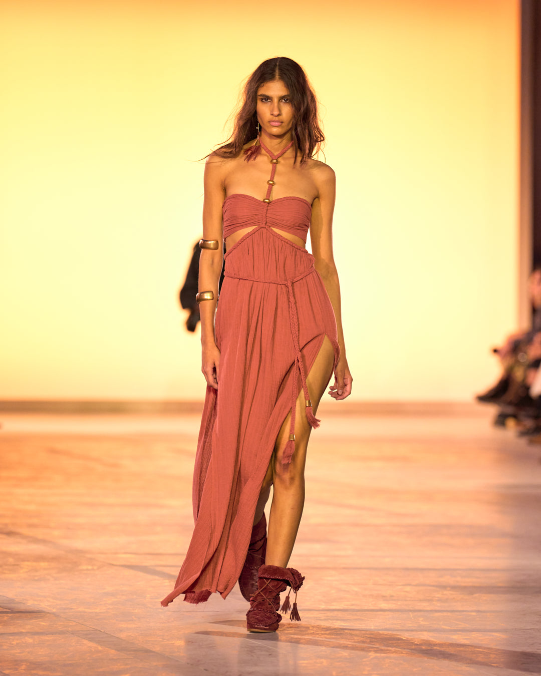 Female model on the catwalk, wearing the Justine long dress in cotton and Winki boots in suede and braided leather in burgundy.
