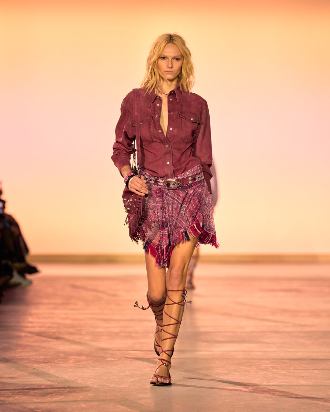 Female model on the catwalk, wearing the Danisia shirt in raspberry suede, the Dova draped skirt in pink printed elastic tulle, the OSKAN SOFT ZIPPED bag in raspberry leather with studs and bangs and pink sandals.