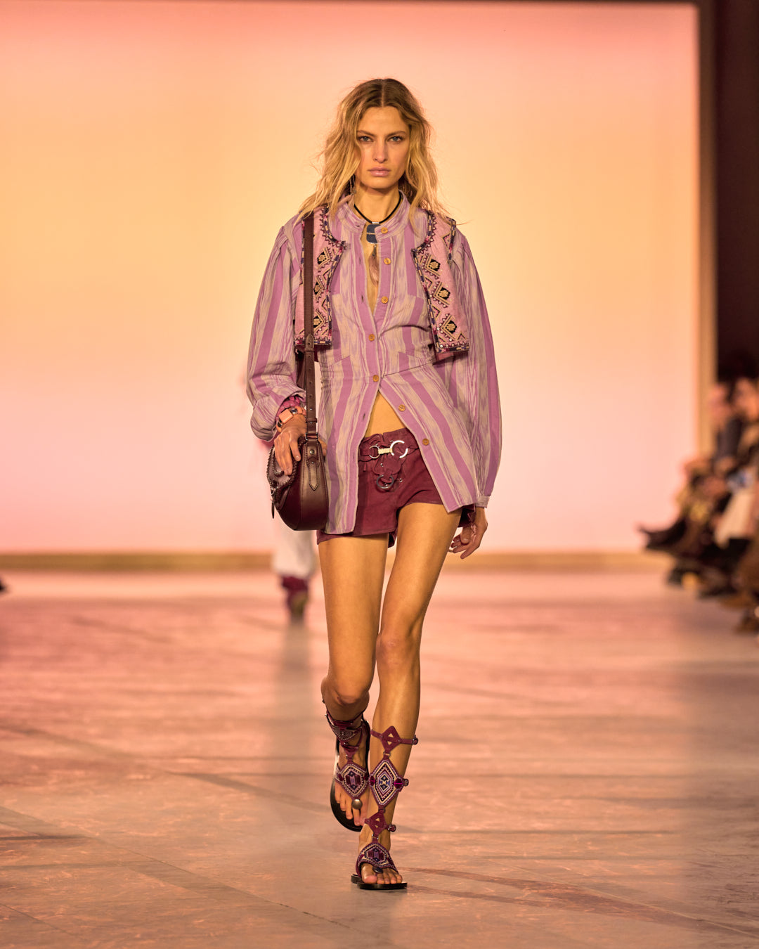 Female model on the catwalk, dressed in a pink striped shirt, Delma lace-up shorts in raspberry suede, altay small bag in burgundy