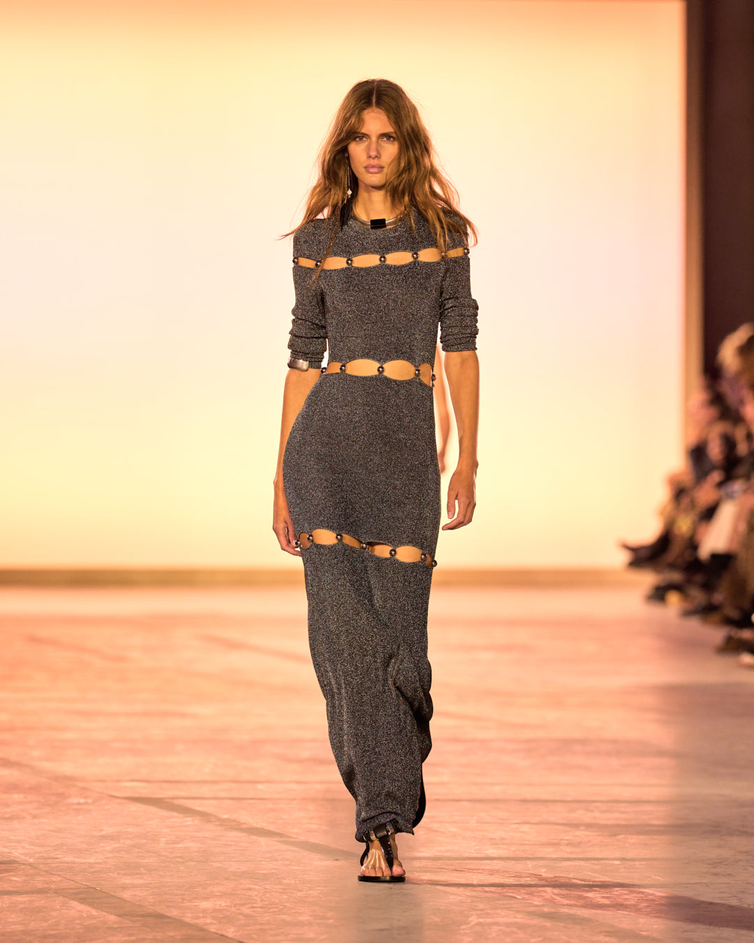 Female model on the catwalk, wearing the Elmire long dress in fine silver mesh and pearls and black sandals.