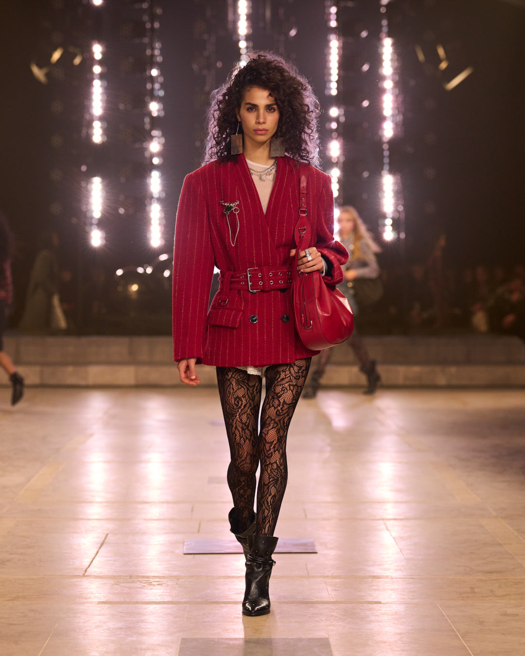 Model walking during the FW25 show with red stripped blazer and red leather bag.