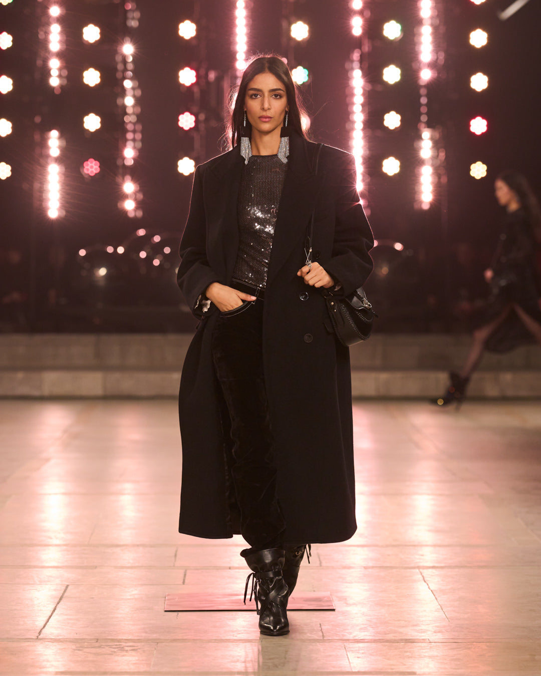 Model walks the FW25 show with a long black coat.