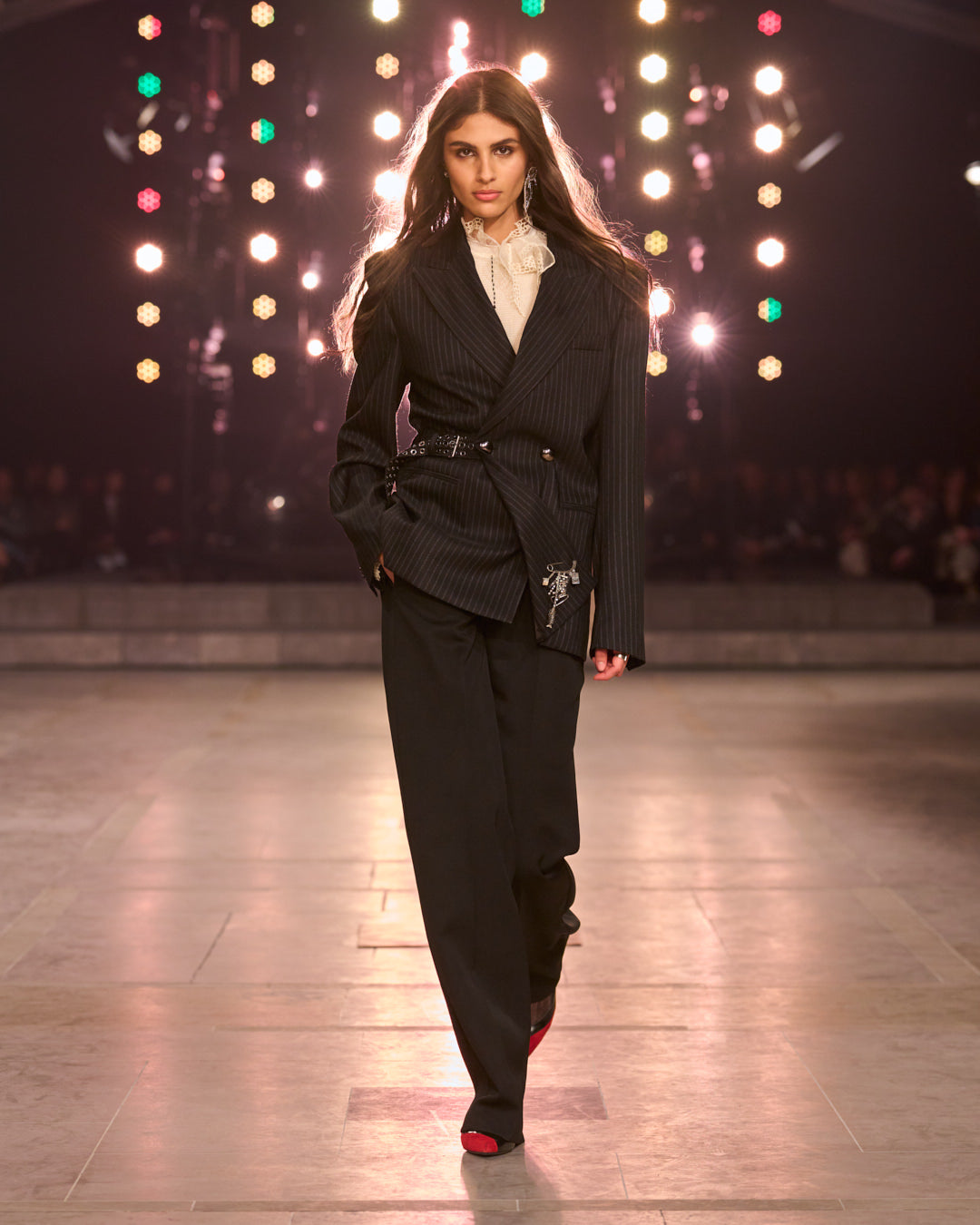 Model wears a striped blazer with laces white shirt and classic tuxedo black pants.