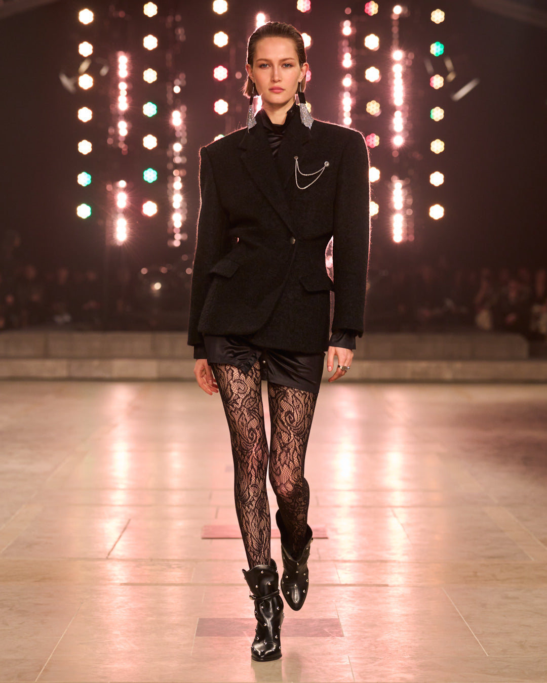 Model wearing black wool jacket with charms silver details, tight with motifs as laces.